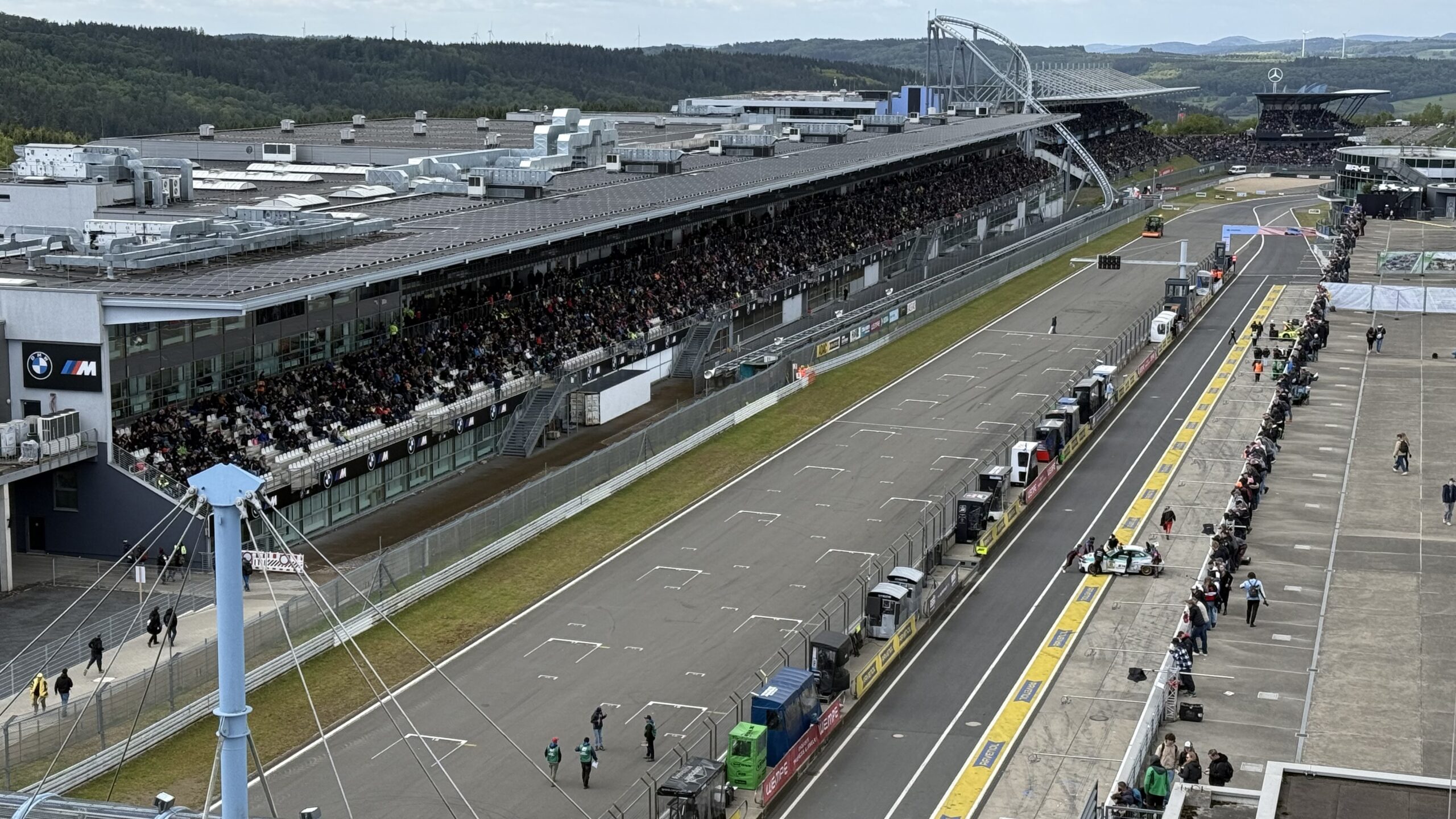 Blick auf die Rennstrecke des Nürburgrings mit vollbesetzten Tribünen und Teamboxen vor dem Start