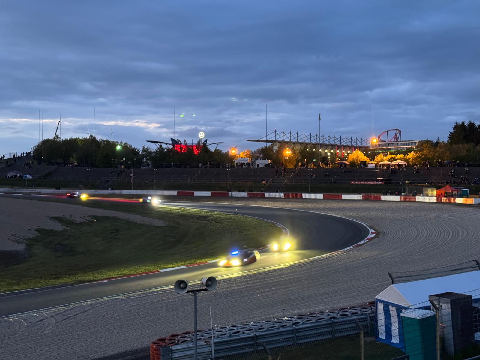 Rennwagen mit leuchtenden Scheinwerfern während der Abenddämmerung auf der Nürburgring-Strecke